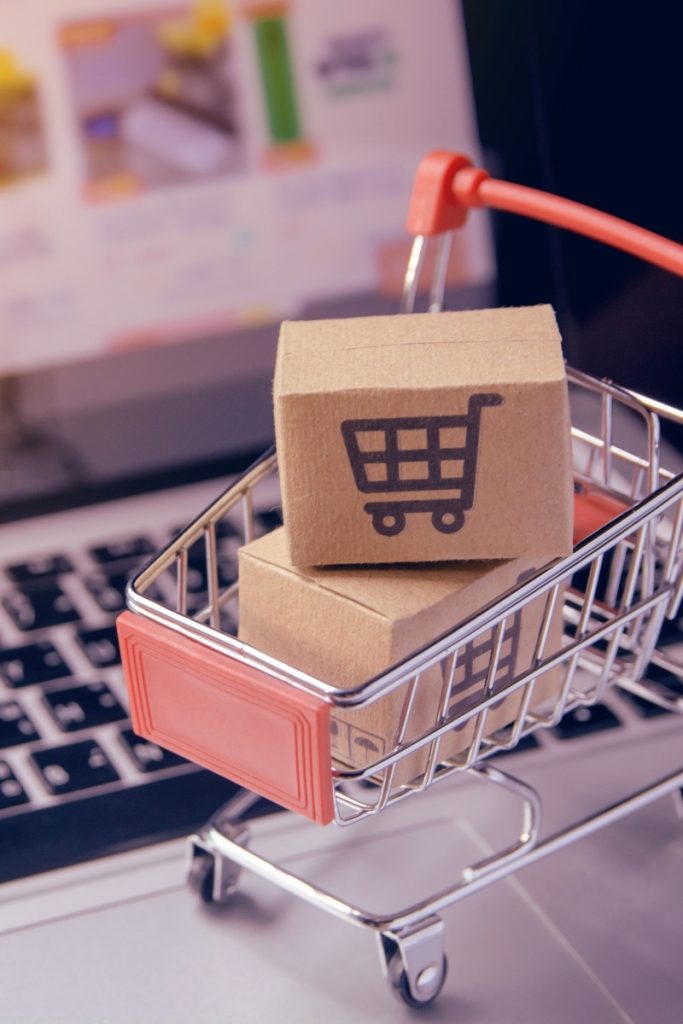 Miniature shopping cart with parcels resting on a laptop keyboard